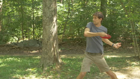 A-Man-Throwing-a-Driver-at-the-Beginning-of-a-Round-of-Disc-Golf-in-a-Wooded-Course,-Slow-Motion