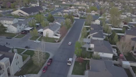 drone-view-of-car-driving-in-suburban-neighborhood-in-evening-pulling-back-revealing-mountains