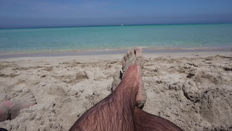 Man-relaxing-barefoot-on-the-beach-looking-at-he-sea-|-POV