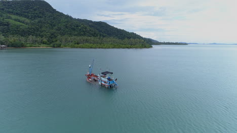 Impresionante-Toma-Aérea-De-Un-Barco-De-Pesca-Que-Se-Hunde-Frente-A-La-Costa-De-Una-Isla-Montañosa-En-Tailandia
