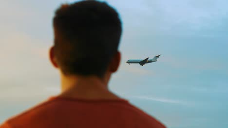 In-this-footage-you-can-see-profile-picture-of-the-male-person-looking-at-airplane-landing-in-the-evening-sky
