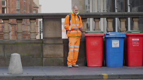 Mann-In-Warnschutzkleidung-Stand-Neben-Mülleimern-Und-Vorbeigehenden-Leuten