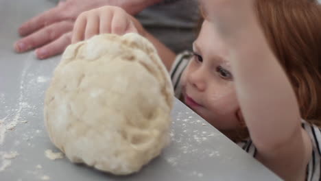 Pre-school-girl-with-a-handful-of-dough-and-a-face-full-of-flour-helping-Mom-make-a-make-in-the-kitchen