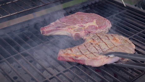 Raw-steaks-grilling-on-a-charcoal-barbecue-while-seared-on-one-side