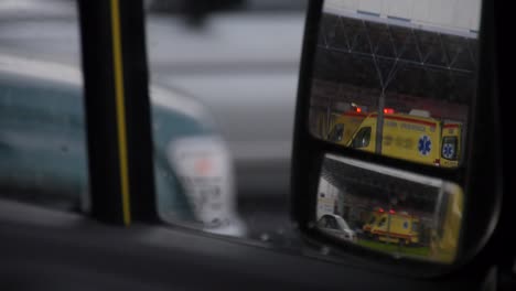 View-of-an-ambulance-with-flashing-lights-as-seen-through-a-rear-view-mirror
