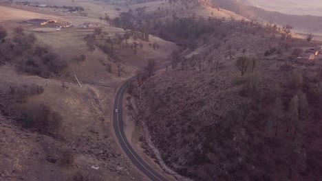 Aerial-view-of-car-driving-through-mountain-road-at-golden-hour