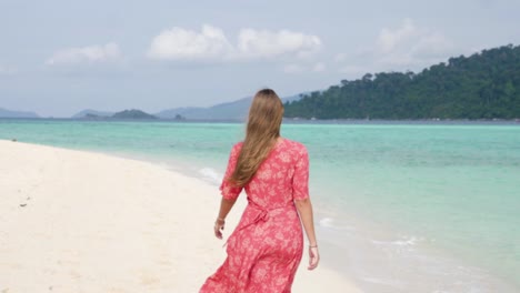 Ultra-slow-motion-shot-of-brunette-woman-in-pink-dress-walking-away-from-camera-on-beautiful-beach-on-island-in-Thailand