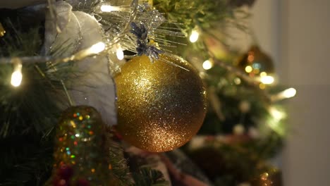 Close-up-of-gold-glittering-Christmas-ornaments-on-a-lit-Christmas-tree