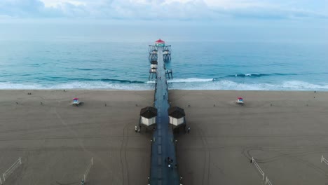 A-4k-ariel-view-moving-towards-the-Huntington-Beach-pier-in-California-Surf-City-USA-at-sunrise-as-surfers-catch-waves-and-families-enjoy-their-travel-and-vacations-at-the-beach