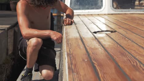 Young-man-sanding-timber-on-wooden-boat-by-hand