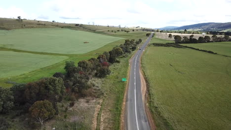Drone-Shot-Of-Car-Driving-Off-Into-Distance-Along-Straight-Country-Road-Lined-By-Trees