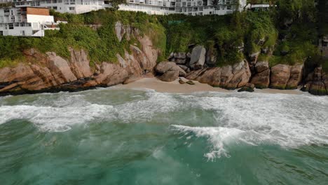 Slowly-backing-away-from-the-cliff-rocks-of-Joatinga-beach-in-Rio-de-Janeiro-during-high-tide-revealing-the-green-ocean-waves-rolling-in