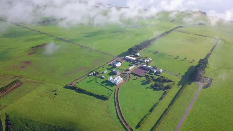 Aerial-flight-over-green-field-and-farmhouse-above-clouds-in-Tasmania,-Australia