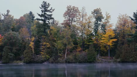 Spooky-mist-floats-over-the-lake-during-a-gloomy-fall-day-in-a-colorful-forest
