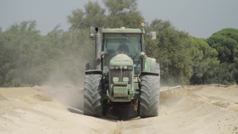 Tractor-plowing-dirt-with-grading-blade-on-farm-driving-toward-camera,-SLOWMO