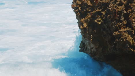 Ocean-waves-with-foam-splashing-against-coral-boulder,-Detail-Shot