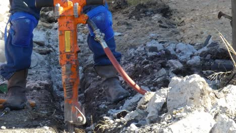 Man-clearing-debris-with-shovel-in-trench-by-his-jack-hammer-close-up-camera