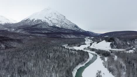Drone-Pulls-away-from-mountain-range-along-Alaskan-frozen-river