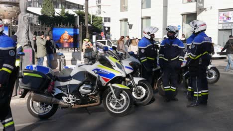 Five-police-officers-in-a-blue-uniform-gather-in-front-of-their-motorbike-parked-to-block-the-street-to-talk-while-a-yellow-jacket-protester-awaits-the-beginning-of-the-demonstration