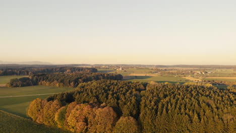 Aerial-clip-of-the-Bavarian-plain,-with-a-forest-in-the-foreground-and-a-road,-with-cars-moving,-in-the-background