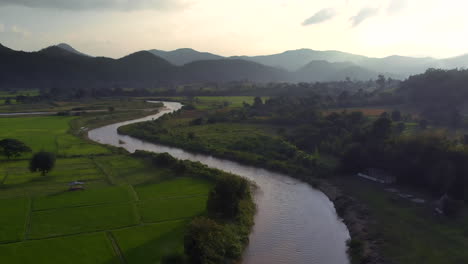 Aerial-flight-above-river-and-Rice-fields-against-mountains-on-horizon-during-sunset-time