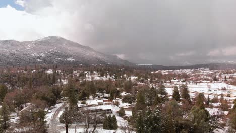 Aerial-Flyover-Small-Town-Nestled-in-Mountains-and-Pine-Trees-During-Snowfall