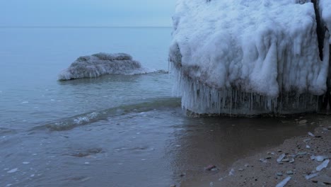 Small-waves-breaking-against-the-ruins-of-Karosta-Northern-Forts-fortification-on-the-shore-of-Baltic-sea-on-a-cloudy-winter-day,-covered-with-ice,-snow-and-icicles,-medium-shot