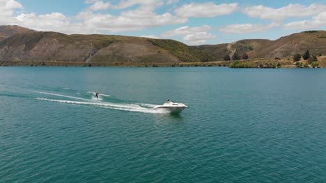 SLOWMO---Waterskiing-behind-boat-on-Lake-Dunstan-near-Clyde-dam,-Central-Otago,-New-Zealand-with-mountains-and-clouds-in-background