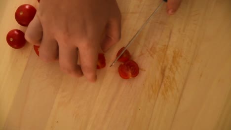 Weibliche-Hand-Schneidet-Mit-Einem-Messer-Winzige-Saftige-Tomaten-Auf-Einem-Hellen-Holzschneidebrett