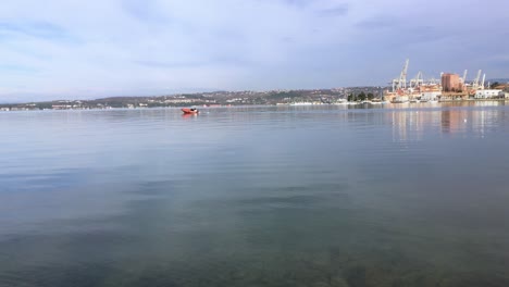 Rotes-Schlauchboot-Mit-Motor-Auf-Ruhiger-See-Mit-Hafen-Und-Kränen-Im-Hintergrund