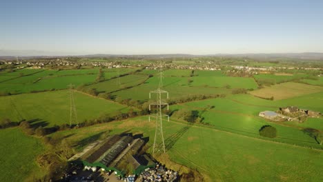 Aerial-footage-of-high-voltage-electricity-towers-and-power-lines-in-the-beautiful-Staffordshire-countryside,-agricultural-fields-and-farms