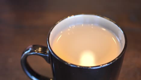 In-Einem-Café-Aufgenommener-Clip-Einer-Schwarzen-Und-Braunen-Kaffeetasse-Mit-Heißem-Kaffee-Oder-Tee-Darin-Und-Lichtreflexion-In-Einer-Flüssigkeit