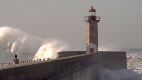 ocean-big-waves-crash-over-the-lighthouse-with-a-person-in-the-foreground