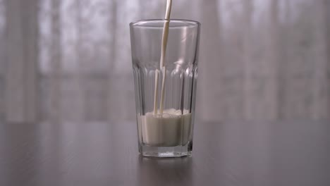 Pouring-cow-milk-into-tall-glass-in-slow-motion,-straight-ahead-shot