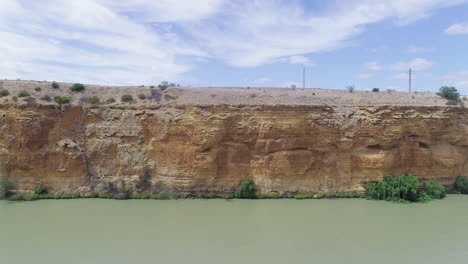 Aerial-shot-of-beautiful-orange-limestone-cliffs-towering-over-the-stunning-Murray-River-in-South-Australia