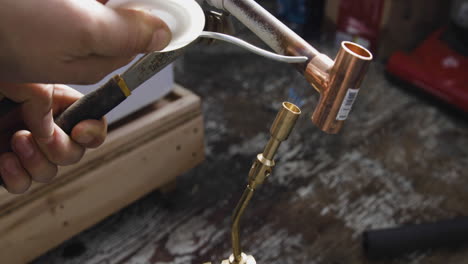 A-copper-tee-fitting-is-welded-to-a-pipe-using-solder,-a-propane-blow-torch-and-an-adjustable-wrench