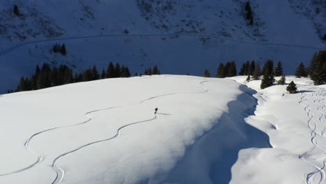 Aerial-shot-tracking-a-snowboarder-off-piste,-in-fresh-snow-and-sunshine-along-a-snowy-ridge-in-the-French-Alps-in-winter