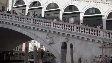 Famous-Italian-landmark,-the-Rialto-bridge-with-tourists-visiting---boats---Gondolas-passing-below