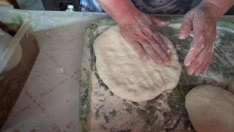 Woman-bare-hands-making-dough-to-a-flat-georgian-bread-on-a-plastic-board-with-flour,-top-shot