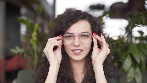 Smiling-young-woman-brushes-the-hair-out-of-her-face,-looks-at-the-camera,-and-puts-on-a-pair-of-glasses