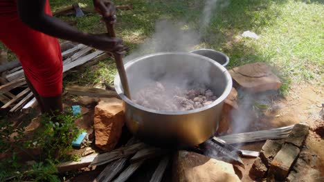 African-woman-stirring-big-pot-of-meat-on-top-of-wood-fire