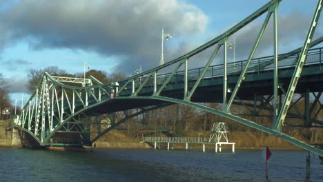 Cars-driving-over-the-Oskara-Kalpaka-Metal-Swing-Bridge-at-Liepaja-in-sunny-afternoon,-wide-shot