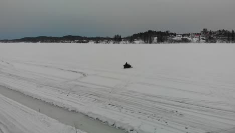Tracking-aerial-shot-of-a-man-driving-his-snowmobile-on-Indalsalven-in-Timra,-Sundsvall,-Sweden