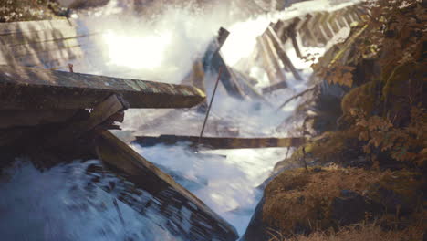 Rushing-Water-Rapids-Flowing-Down-Log-Chute-and-Crashing-Into-Damaged-Wooden-Beams-with-Mossy-Rocks-During-Autumn-4K-ProRes