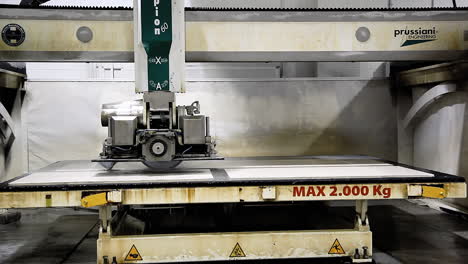 A-cutting-bench-at-a-countertop-factory,-with-an-automated-machine-saw-cutting-a-granite-block-in-the-middle-while-releasing-a-flow-of-cooling-water