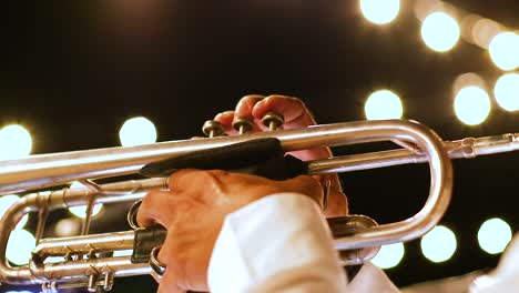 Close-up-of-adult-male-playing-the-trumpet-at-a-show-at-night,-with-bright-lights-in-background