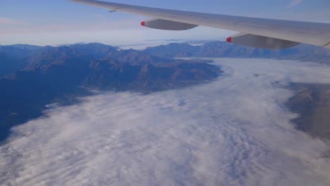Aerial-view-of-mountains-and-flying-above-clouds-with-view-of-airplane-wing