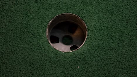 A-close-up-birds-eye-view-of-a-yellow-mini-golf-ball-falls-into-the-golf-hole-and-bounces-in-the-pocket-on-a-course