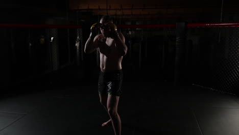 Slow-motion-of-a-mma-fighter,-covered-in-sweat,-in-a-ring,-standing-still-on-the-guard-position,-the-camera-goes-around,-in-a-dark-room,-with-a-single-light