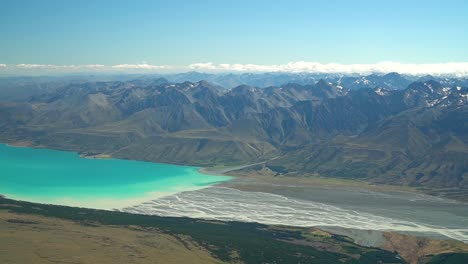 SLOWMO---Aerial-shot-from-plane-scenic-flight-over-braided-rivers-at-Lake-Tekapo,-South-Island,-New-Zealand-with-Southern-Alps-rocky-mountains-in-background